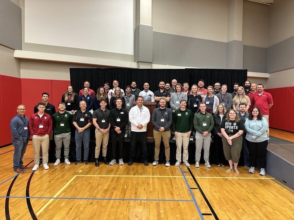 A medium group of people standing inside a gymnasium.
